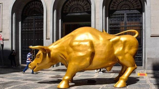 Touro dourado sendo removido por máquinas em frente a prédio