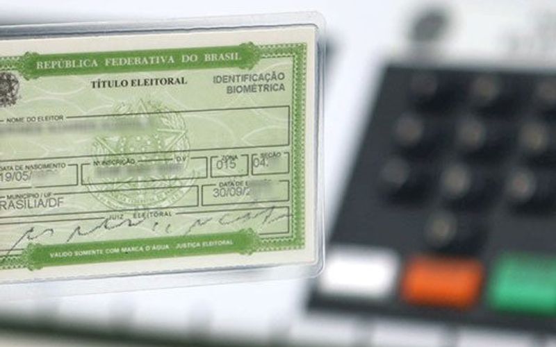 Documento de título de eleitor ao lado de cédula eleitoral oficial