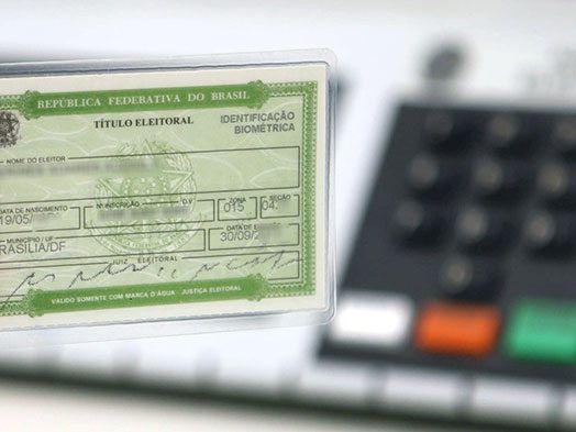 Documento de título de eleitor ao lado de cédula eleitoral oficial