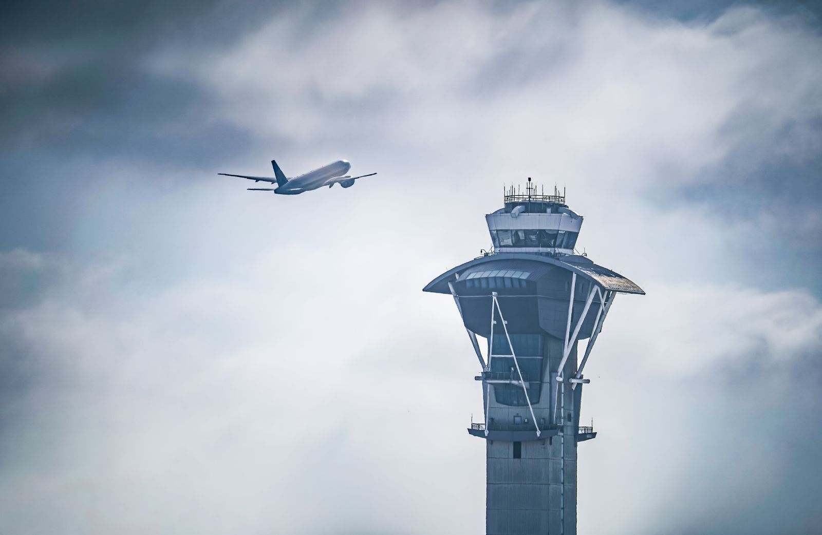 Avião decolando ao lado da torre de controle de tráfego aéreo do aeroporto de Los Angeles (LAX), com céu nublado ao fundo