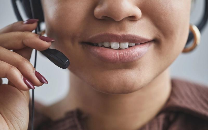 Close da boca de uma mulher sorrindo enquanto fala diante do microfone de um headset.