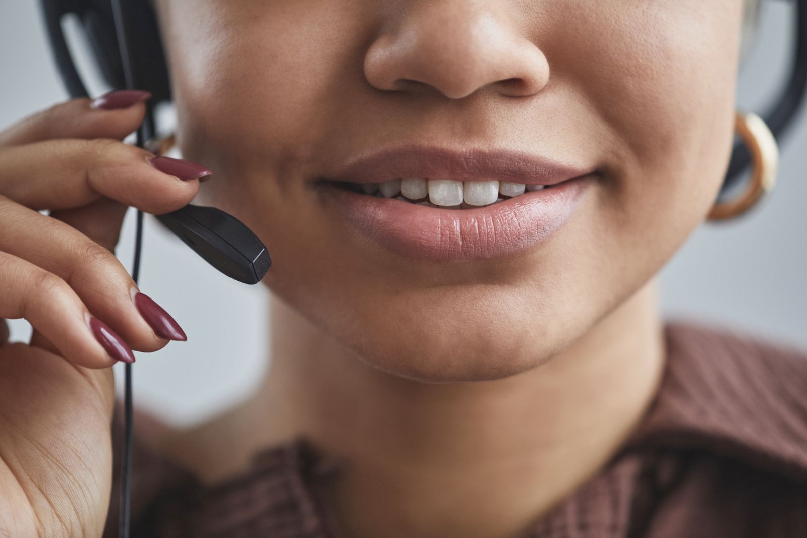 Close da boca de uma mulher sorrindo enquanto fala diante do microfone de um headset.