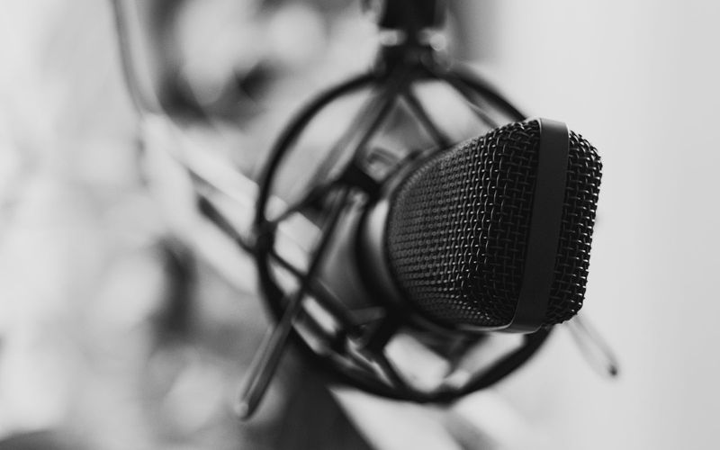 Close-up em preto e branco de um microfone de estúdio com foco seletivo, remetendo ao clima de uma redação de rádio