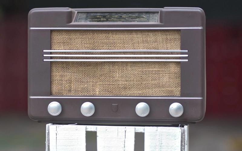 Close de um rádio receptor antigo de madeira, com design retrô, evocando a era de ouro do radiojornalismo brasileiro.