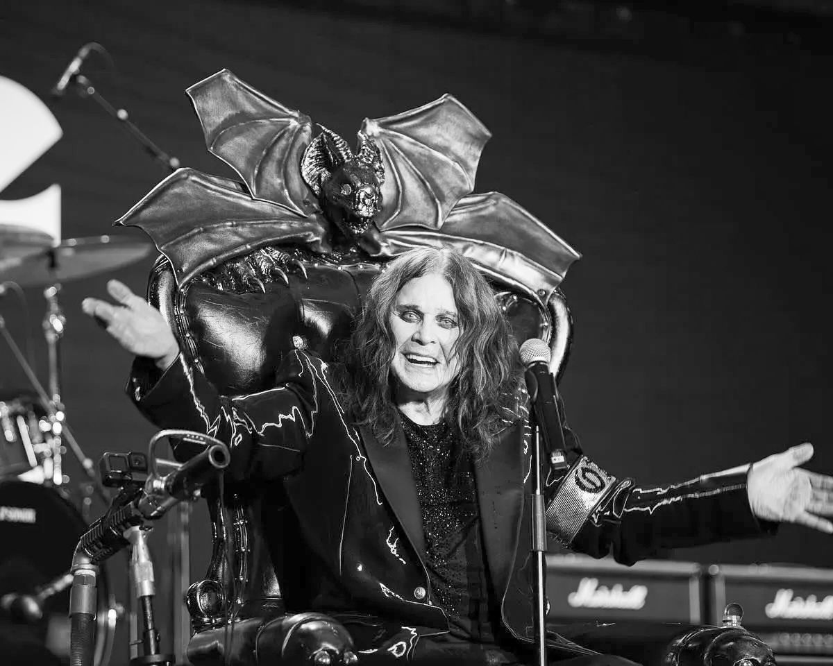 Ozzy Osbourne no palco com roupa característica e microfone em mão