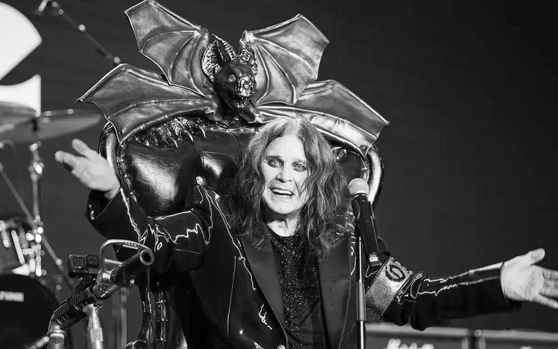Ozzy Osbourne no palco com roupa característica e microfone em mão