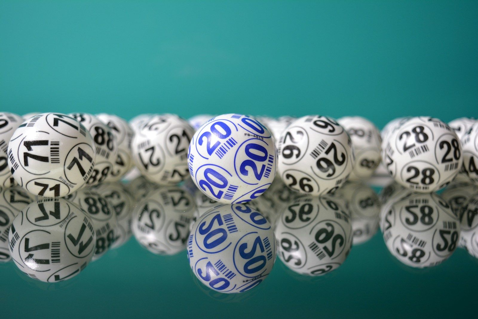 Fileira de bolinhas numeradas de sorteio, brancas com números em azul e preto, refletidas sobre superfície espelhada com fundo verde-azulado