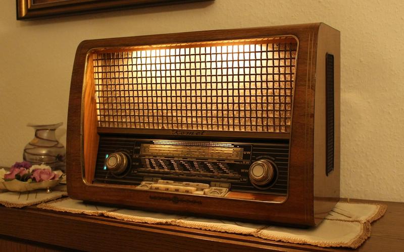 Rádio antigo de madeira com o mostrador iluminado por uma luz dourada e quente, ao lado de rosas secas, criando um clima romântico e nostálgico.