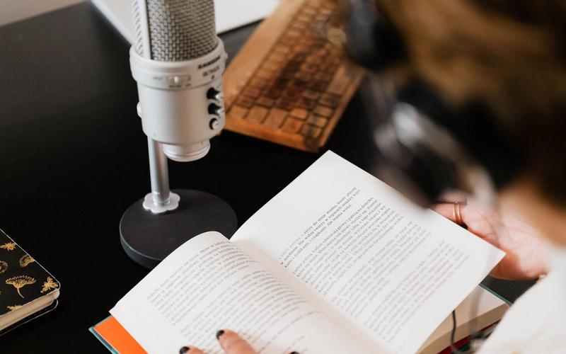 Microfone de estúdio ao lado de um livro aberto sendo lido sobre a mesa, simbolizando a leitura e o cuidado com o português correto na locução de rádio