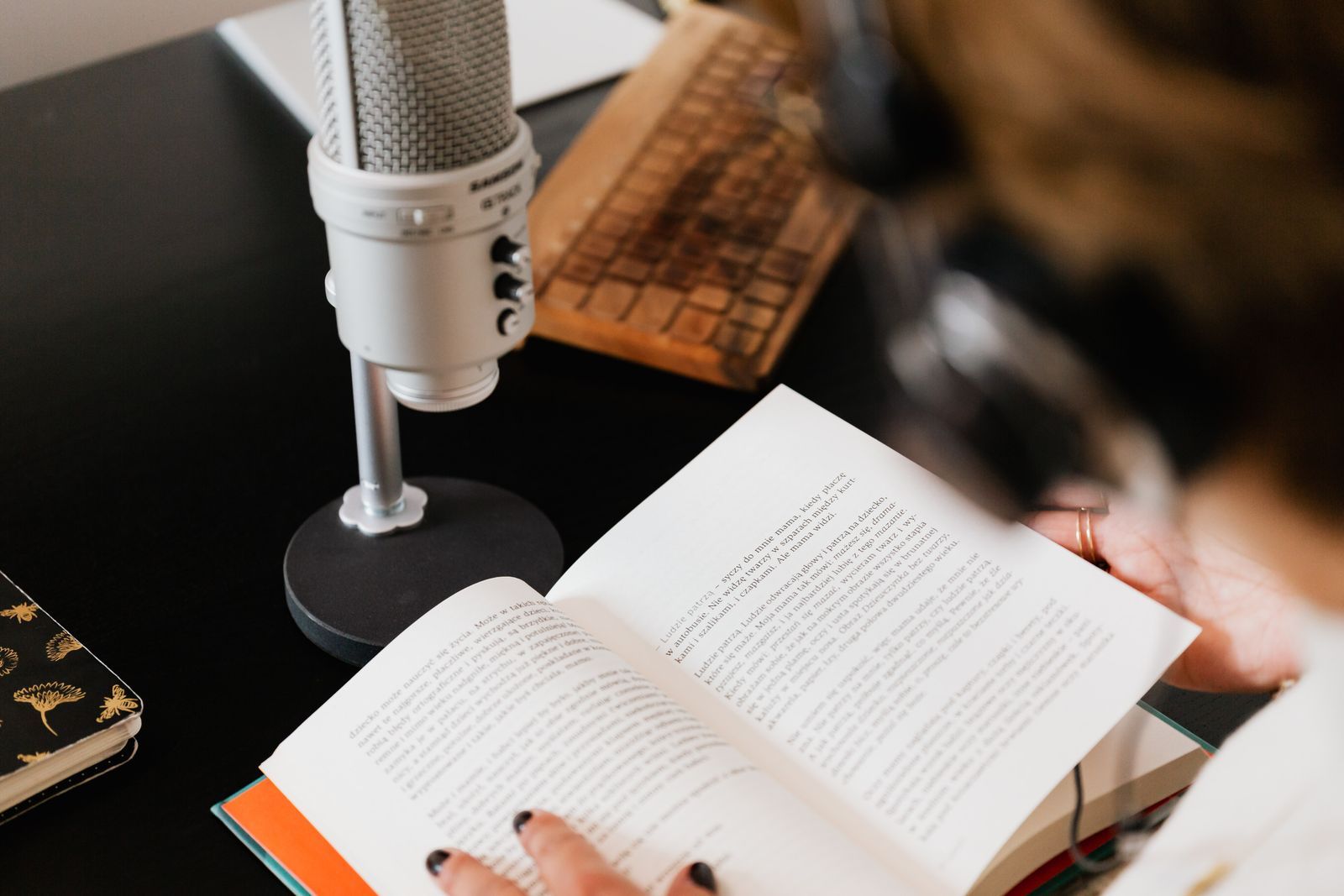 Microfone de estúdio ao lado de um livro aberto sendo lido sobre a mesa, simbolizando a leitura e o cuidado com o português correto na locução de rádio