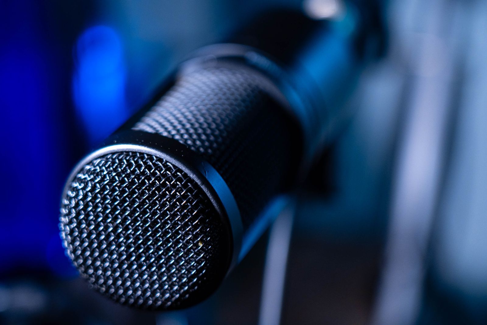 Microfone profissional de estúdio em close, com fundo azul desfocado, evocando a locução e a transmissão de áudio do rádio indoor