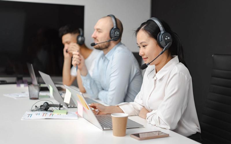 Três atendentes usando headsets trabalham lado a lado em notebooks, em uma central de atendimento telefônico moderna