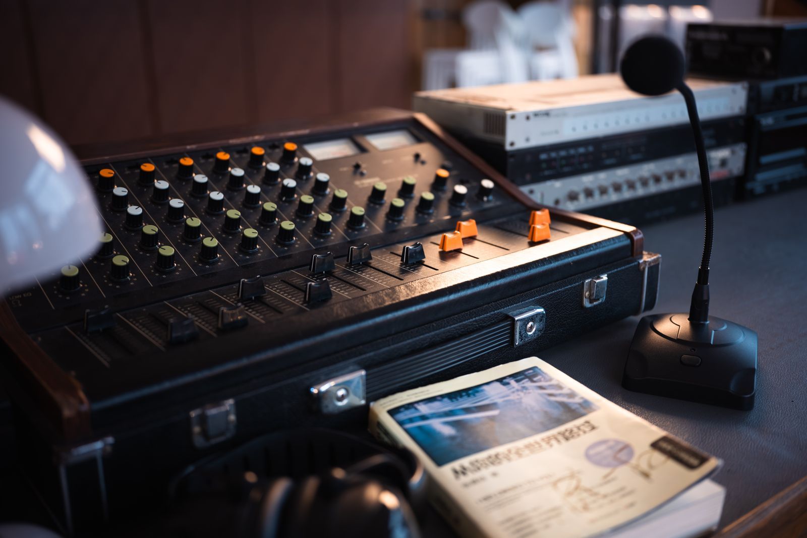 Mesa de controle de um estúdio de rádio antigo, com mesa de som vintage cheia de botões coloridos, um microfone de bancada e equipamentos empilhados ao fundo