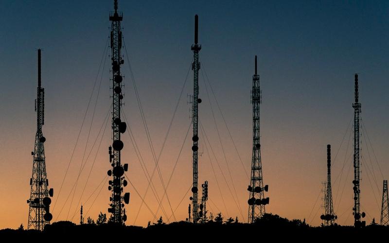 Silhueta de várias torres de transmissão de rádio contra o céu ao pôr do sol, com cabos de sustentação visíveis