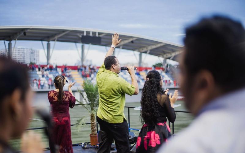 Homem de microfone na mão, com o braço erguido, fala para a arquibancada de um estádio durante um evento ao ar livre