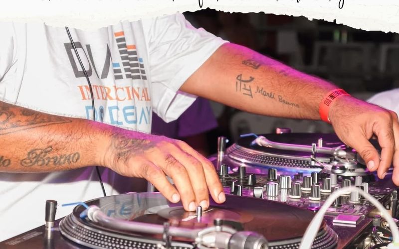 DJ na cabine com headphones, mão em mixer durante apresentação ao vivo.