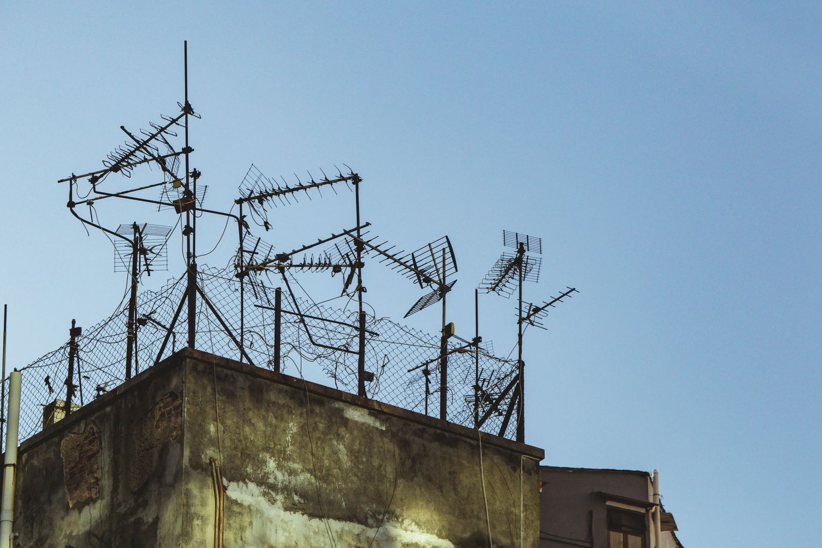 Emaranhado de antenas improvisadas e arame farpado no topo de um prédio antigo, contra um céu azul limpo, remetendo à estética de transmissões de rádio não oficiais