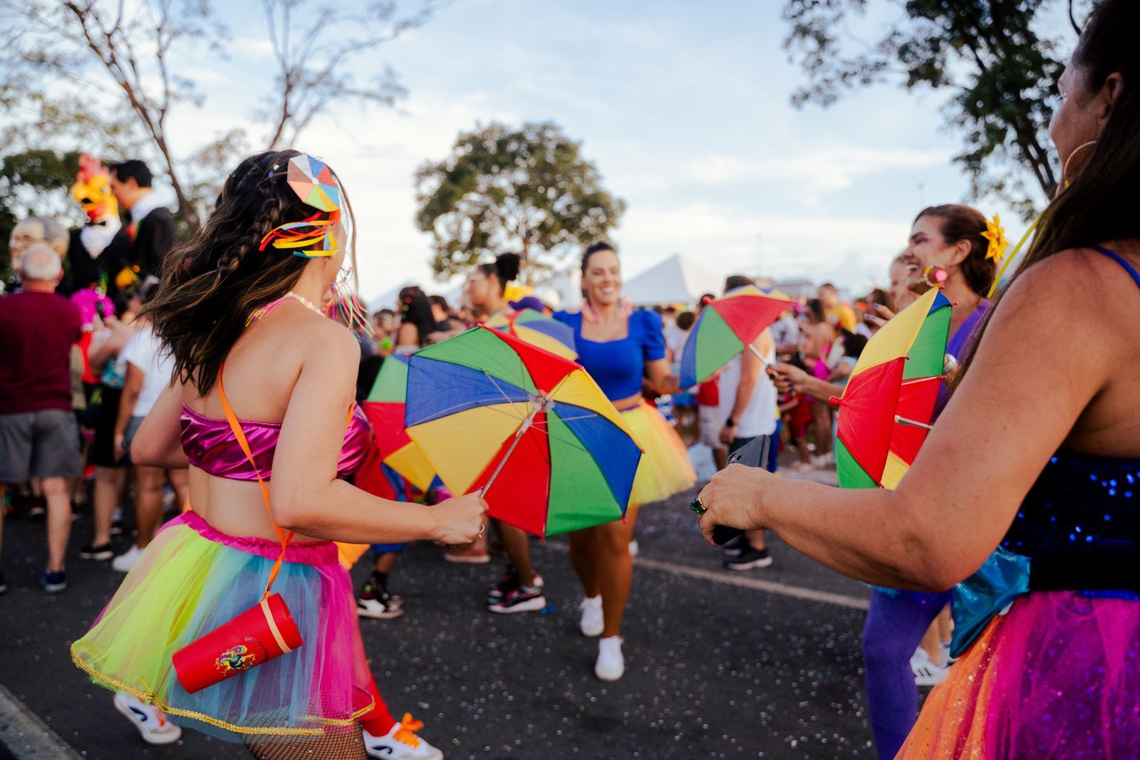 Foliãs dançam com sombrinhas coloridas em bloco de carnaval de rua no Brasil, cercadas por multidão animada ao entardecer