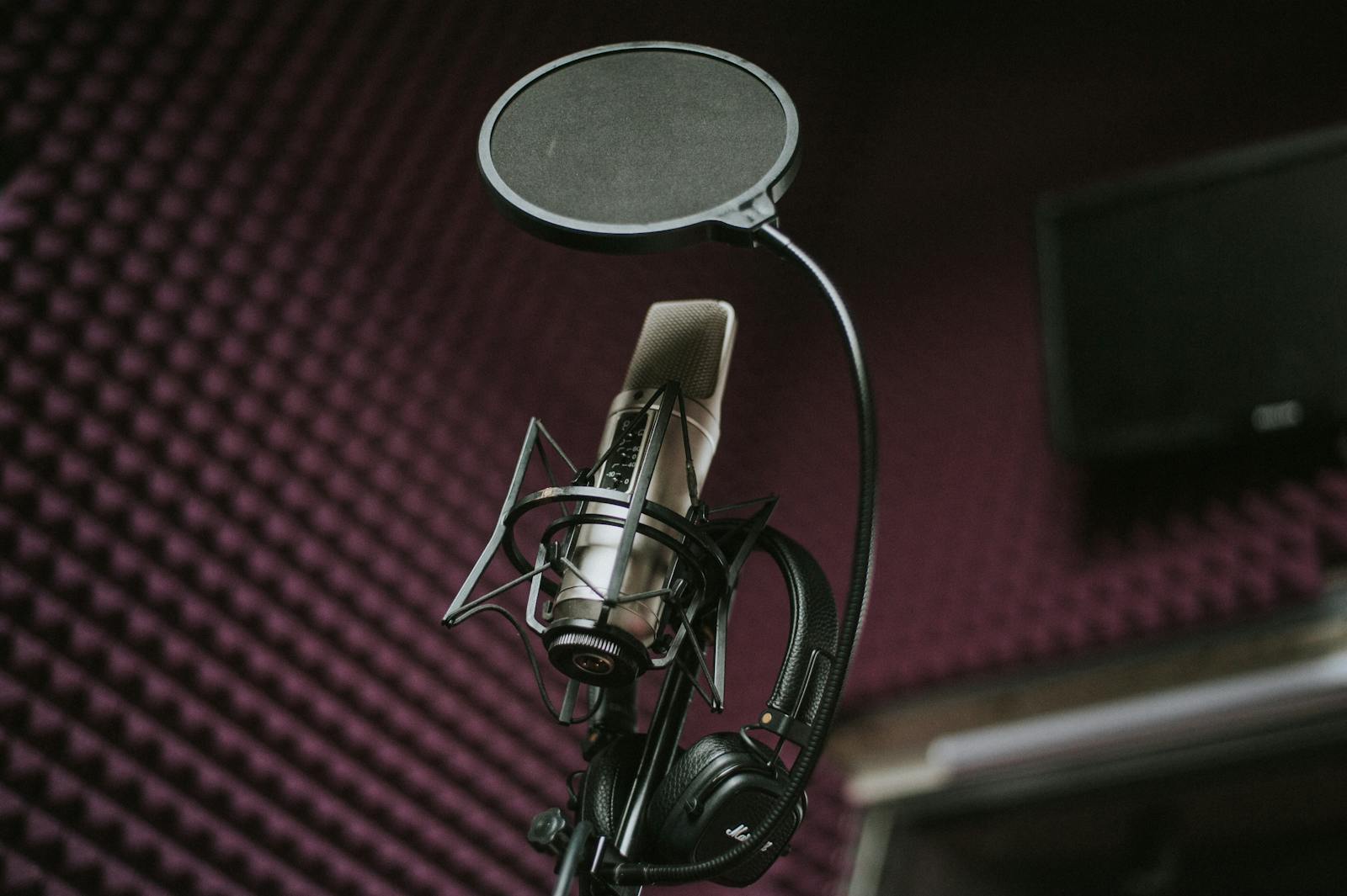 Microfone condensador profissional com filtro pop e fones de ouvido em um estúdio com tratamento acústico, ambiente típico de gravação de narração.