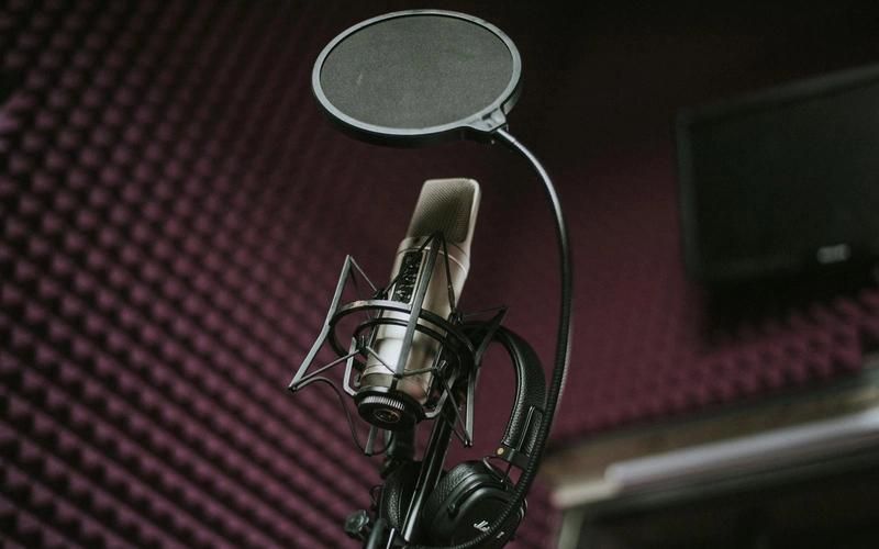 Microfone condensador profissional com filtro pop e fones de ouvido em um estúdio com tratamento acústico, ambiente típico de gravação de narração.
