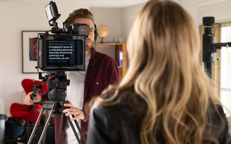 Apresentador em estúdio usando teleprompter durante transmissão ao vivo.