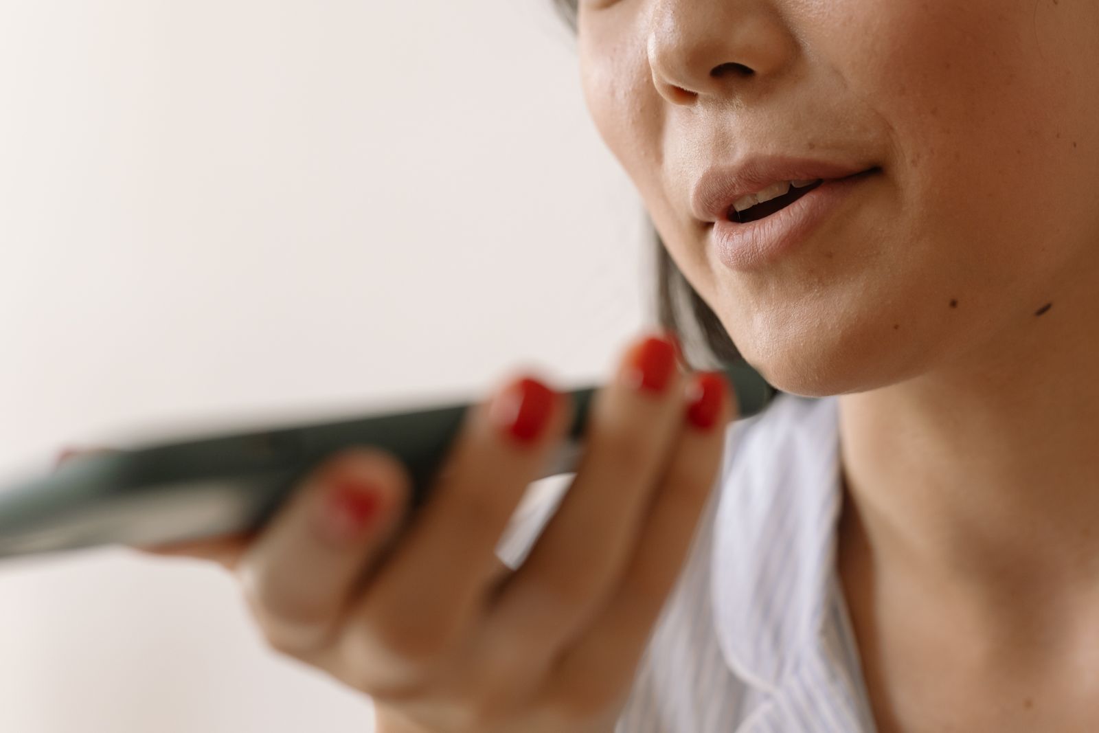 Close-up de uma pessoa falando junto ao microfone do celular, segurando o smartphone próximo à boca para gravar a voz