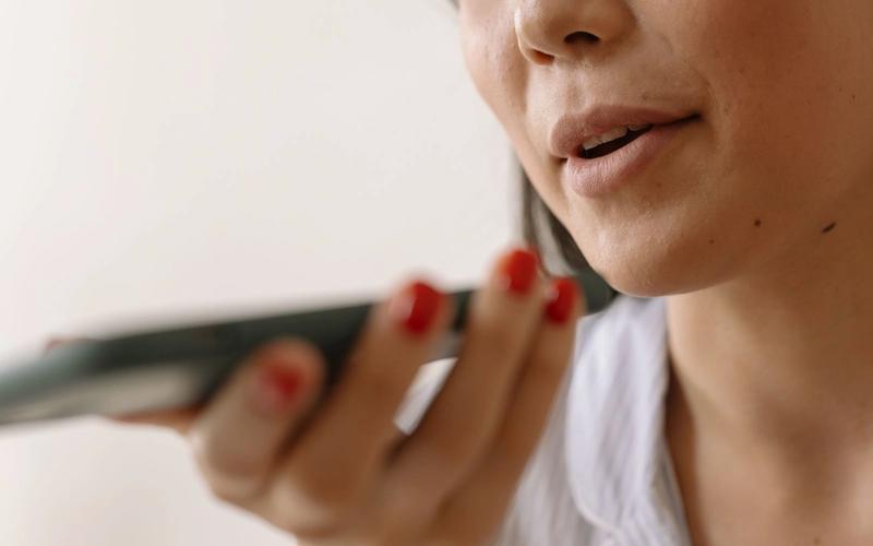 Close-up de uma pessoa falando junto ao microfone do celular, segurando o smartphone próximo à boca para gravar a voz