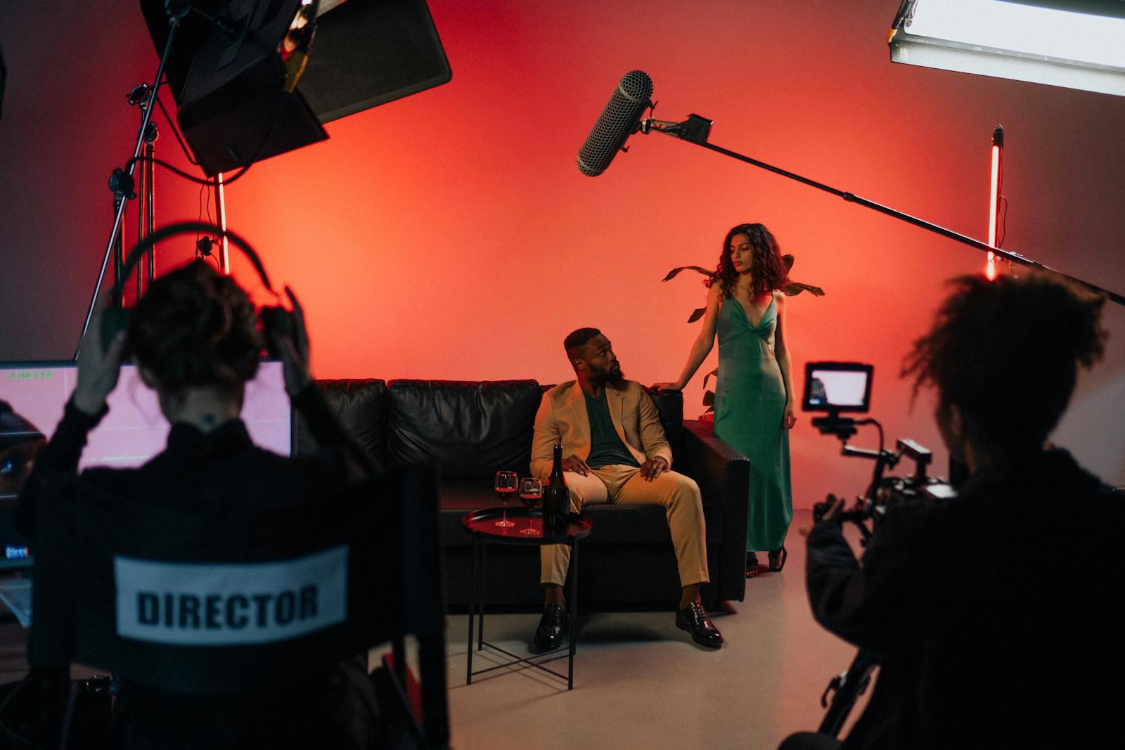 Set de gravação de comercial de TV com atores, diretor, refletores, microfone boom e câmera em estúdio profissional.
