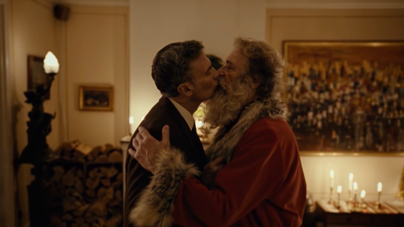 Papai Noel abraçando um homem em cenário natalino ao ar livre