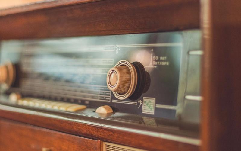 Close-up de um rádio antigo de madeira, com botões dourados e o dial iluminado, evocando a época em que se acompanhavam as Copas do Mundo pela transmissão de rádio