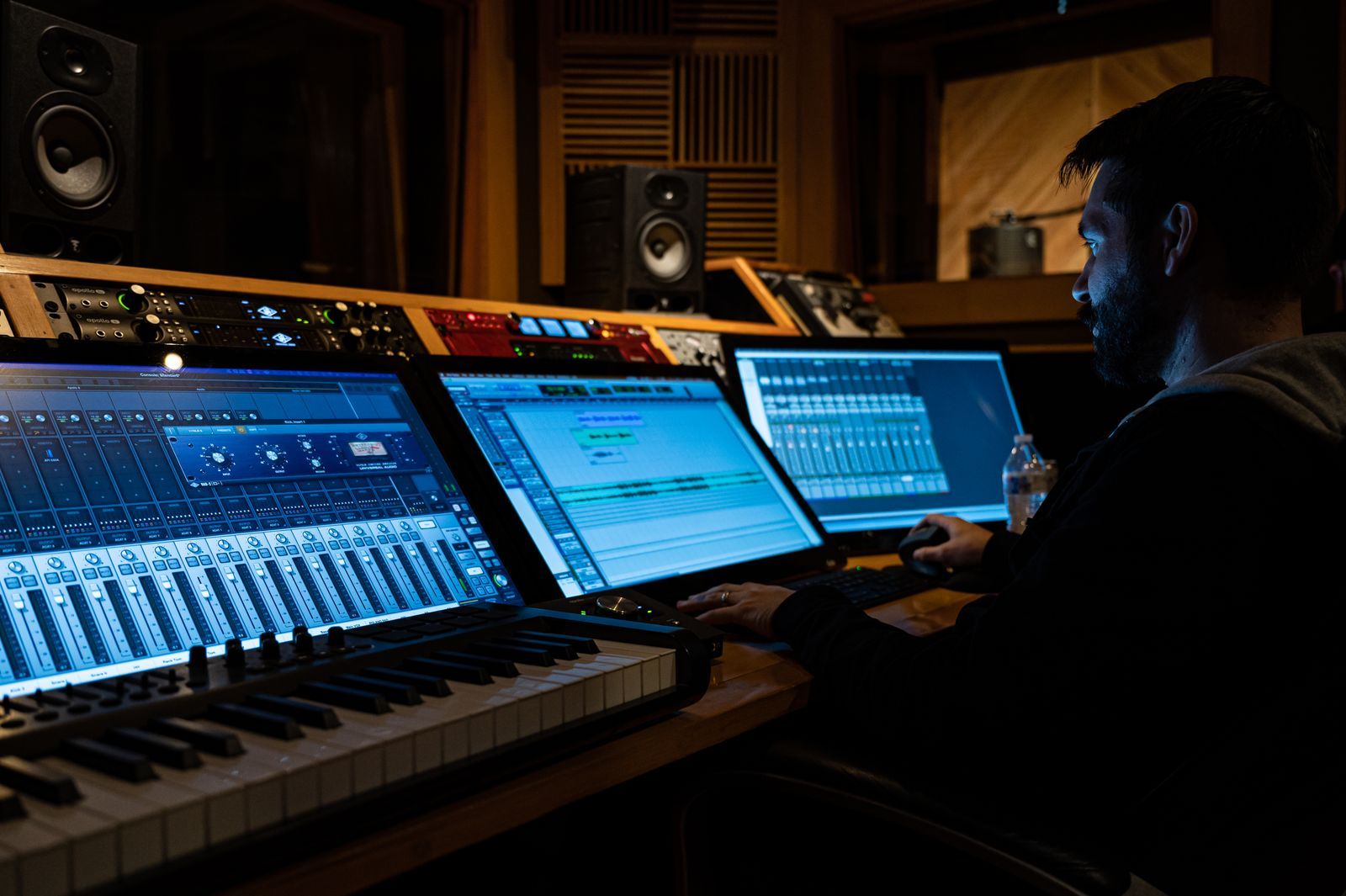 Compositor trabalhando em estúdio de gravação com teclado MIDI, mesa de mixagem e telas de software de áudio, ambiente cinematográfico e iluminação baixa, sugerindo a produção de uma trilha sonora