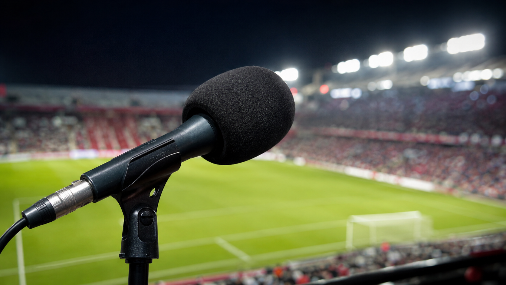 Microfone de transmissão esportiva em primeiro plano, com gramado e arquibancada lotada de um estádio à noite ao fundo, representando a cobertura jornalística da Copa do Mundo 2026