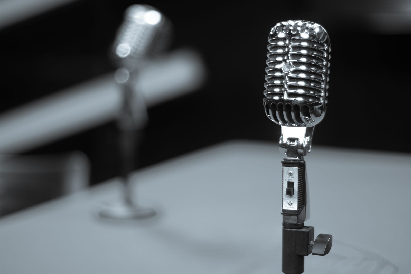 Microfone retrô cromado sobre pedestal em estúdio, em tons de preto e branco, evocando a era de ouro do rádio e da narração esportiva