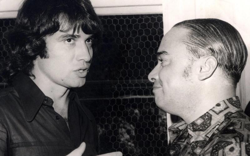 Fotografia em preto e branco de Sérgio Chapelin, jovem, conversando com Haroldo Carvalho Cruz, presidente da Sobeu, na década de 1970