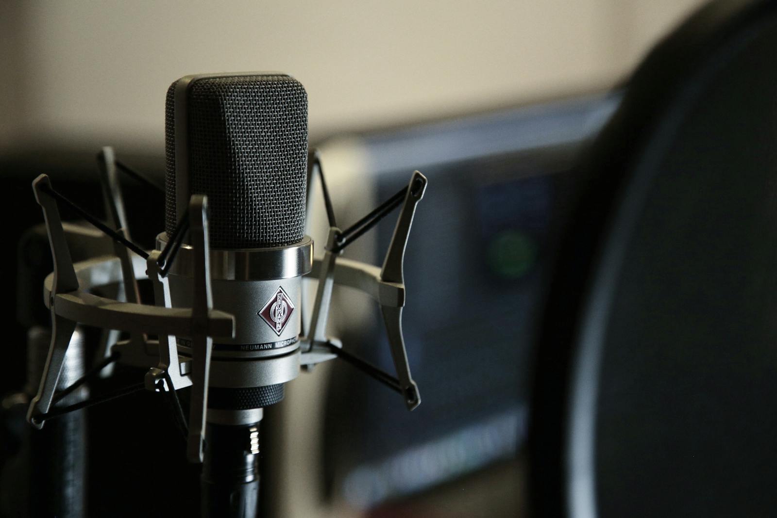 Microfone condensador profissional preto em suporte antivibração, com filtro pop ao lado, em um home studio moderno de gravação de voz.