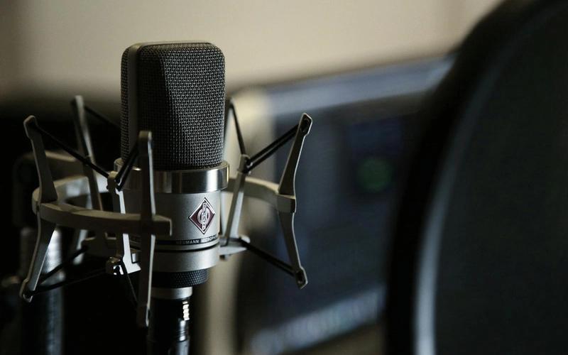 Microfone condensador profissional preto em suporte antivibração, com filtro pop ao lado, em um home studio moderno de gravação de voz.