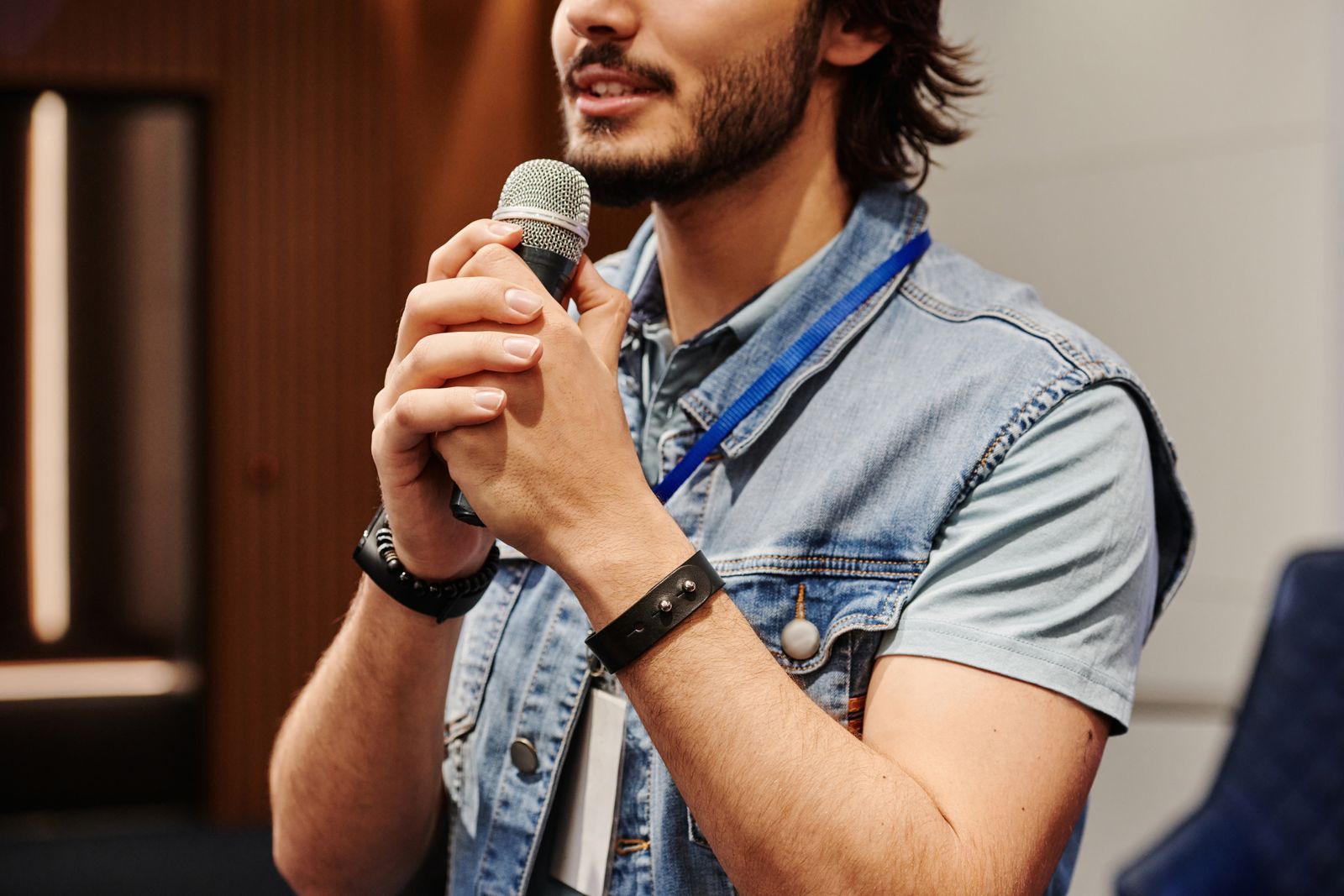 Homem de colete jeans falando ao microfone durante uma apresentação para uma plateia.