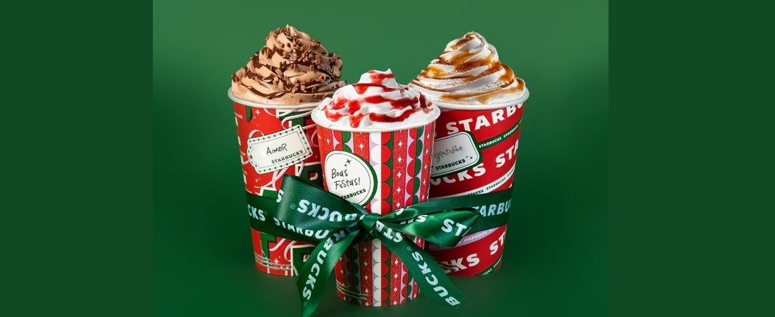 Copo Starbucks de natal com bebida avermelhada entre decoração festiva