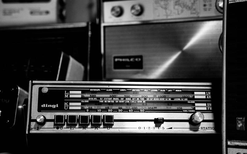 Rádio antigo em preto e branco com mostrador de sintonia exibindo estações internacionais de ondas curtas, com a sigla BBC visível entre os nomes das cidades
