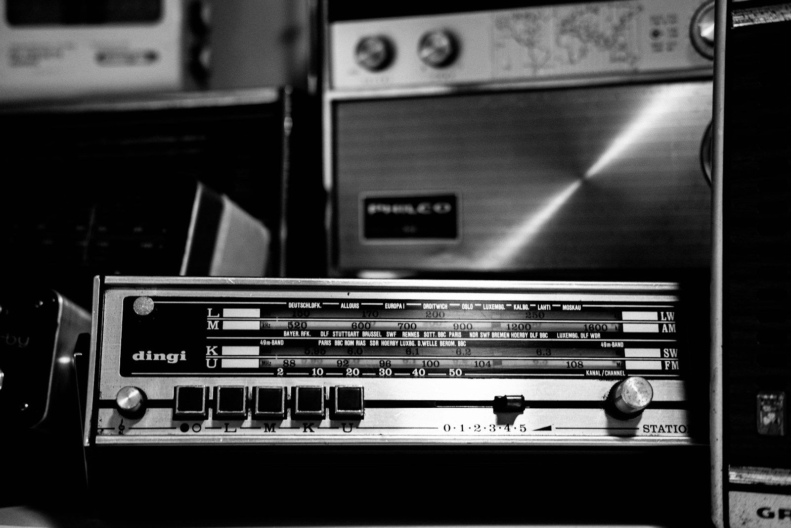 Rádio antigo em preto e branco com mostrador de sintonia exibindo estações internacionais de ondas curtas, com a sigla BBC visível entre os nomes das cidades