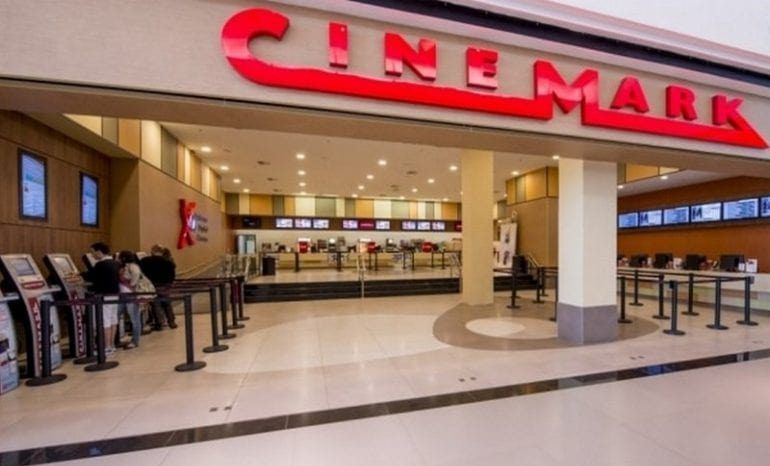 Entrada de cinema com luzes neon e displays de preço em promoção