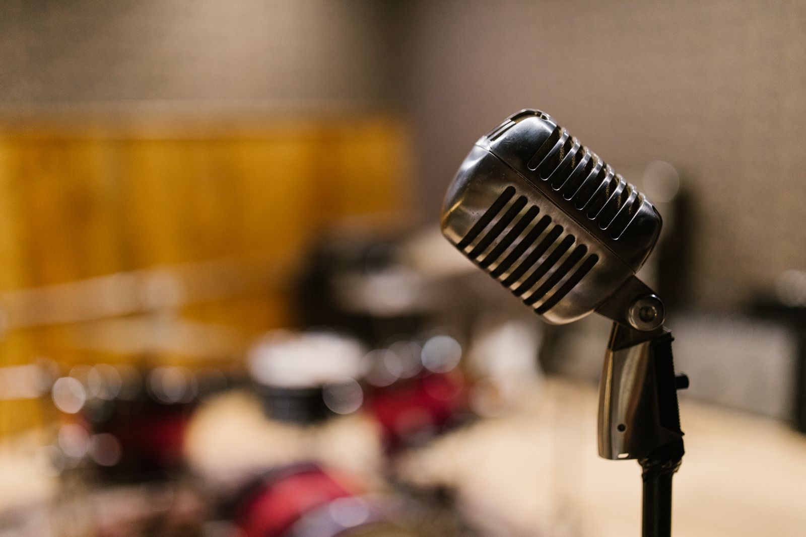 Microfone clássico de rádio cromado em primeiro plano dentro de um estúdio aconchegante, com um segundo microfone de estúdio desfocado ao fundo, evocando a era de ouro do rádio e da TV