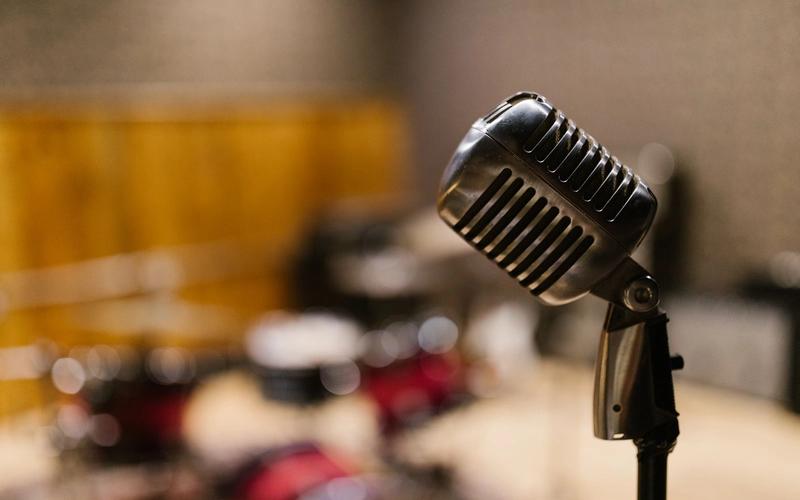 Microfone clássico de rádio cromado em primeiro plano dentro de um estúdio aconchegante, com um segundo microfone de estúdio desfocado ao fundo, evocando a era de ouro do rádio e da TV