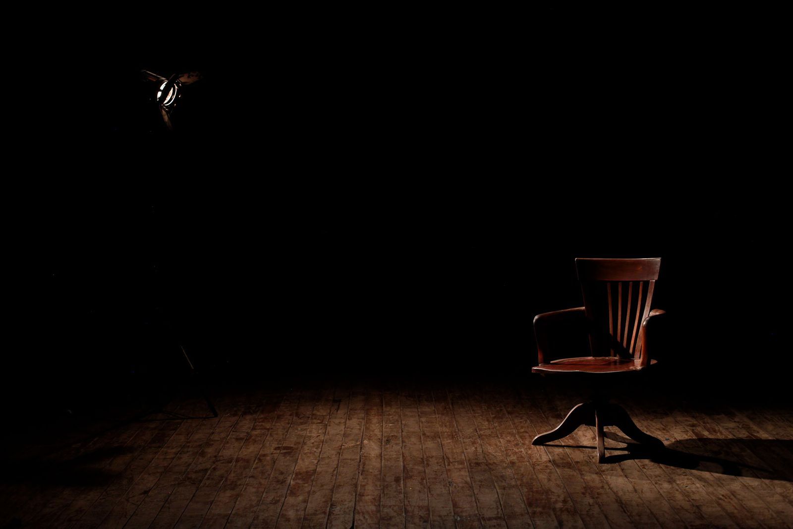 Cadeira de madeira vazia iluminada por um único spot de luz em um estúdio escuro, antes do início da programação
