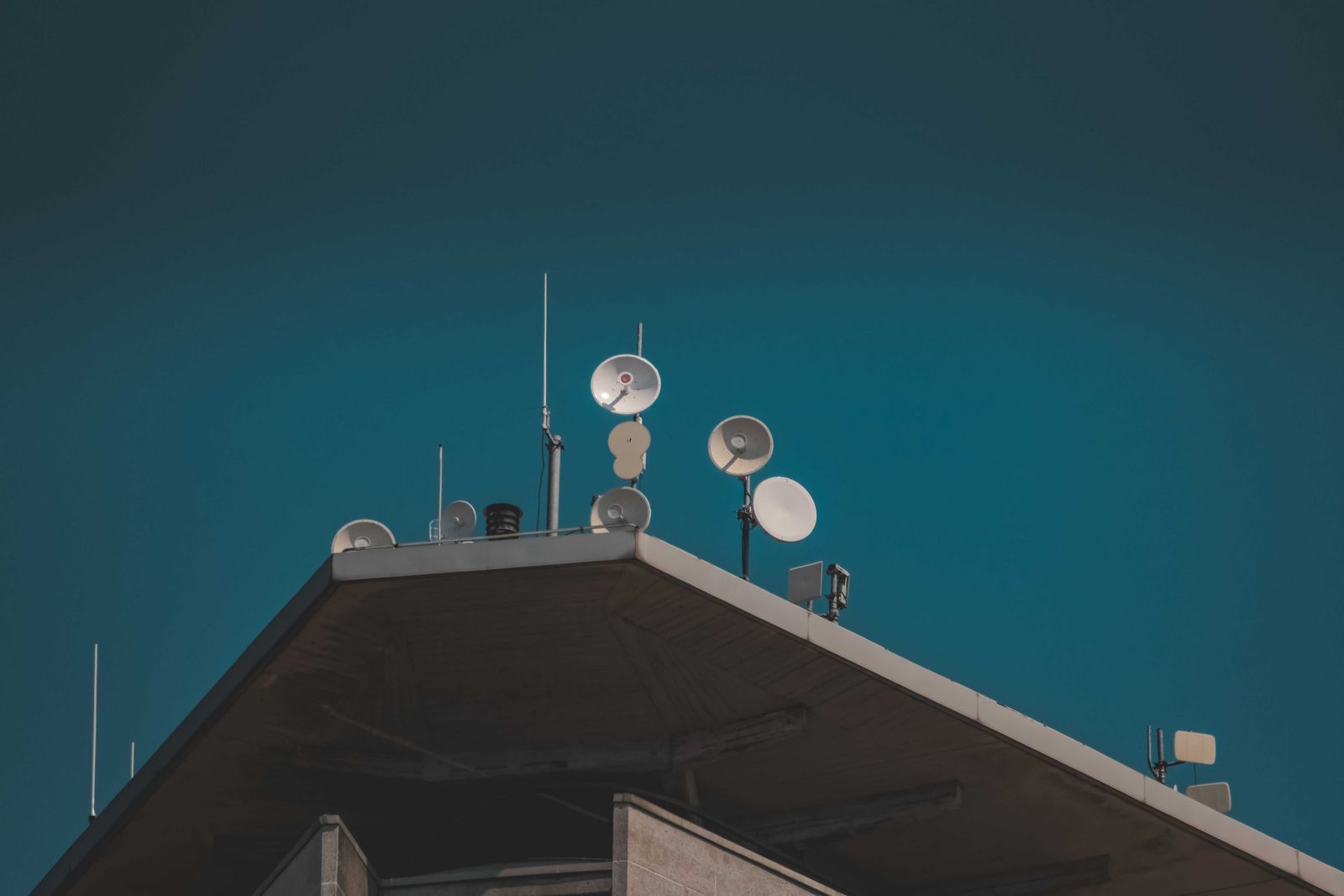 Antenas parabólicas de comunicação no topo de um prédio, contra um céu azul profundo, simbolizando a transmissão via satélite