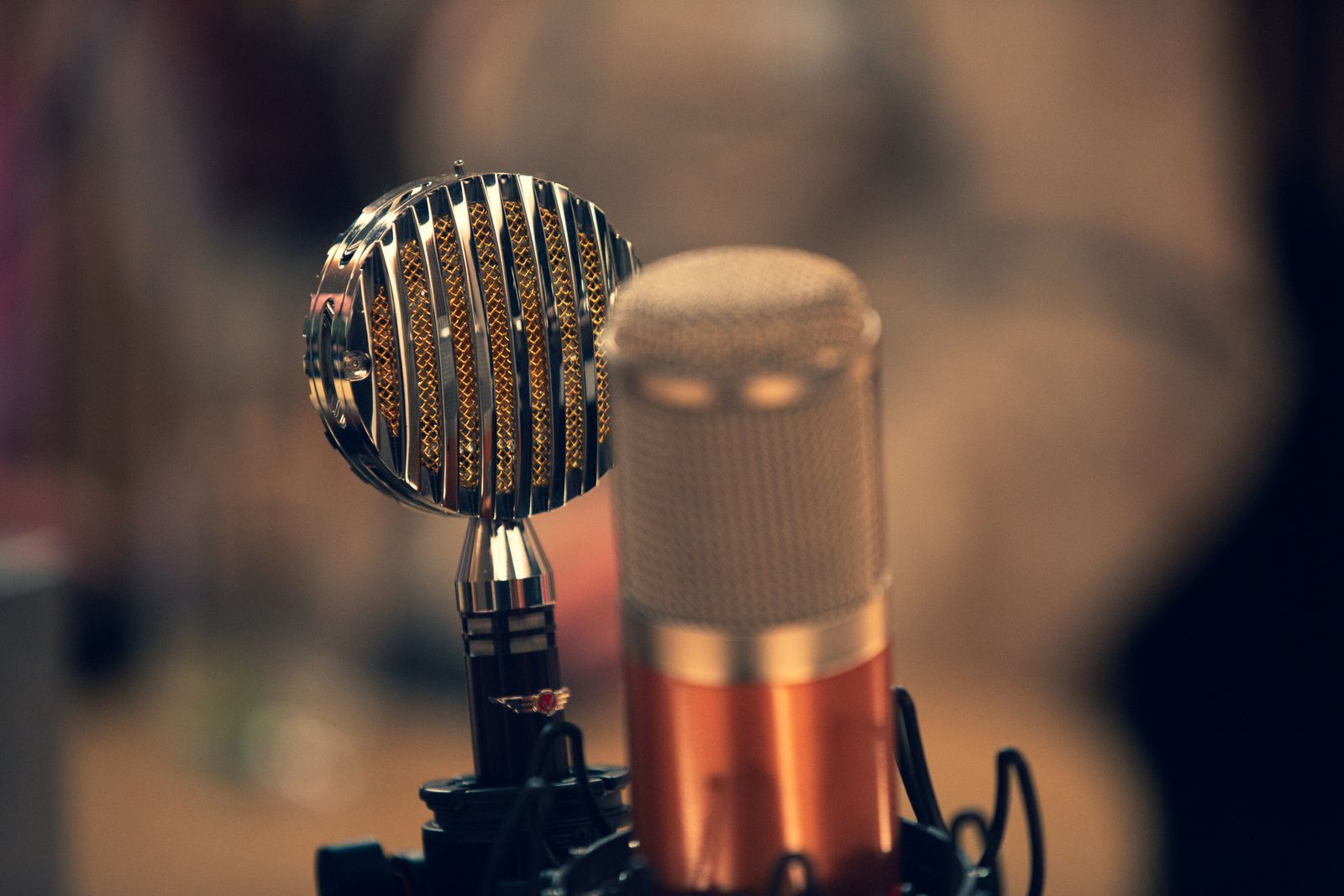 Close-up de um microfone de fita vintage prateado ao lado de um microfone condensador moderno em estúdio de gravação, com iluminação quente e fundo desfocado