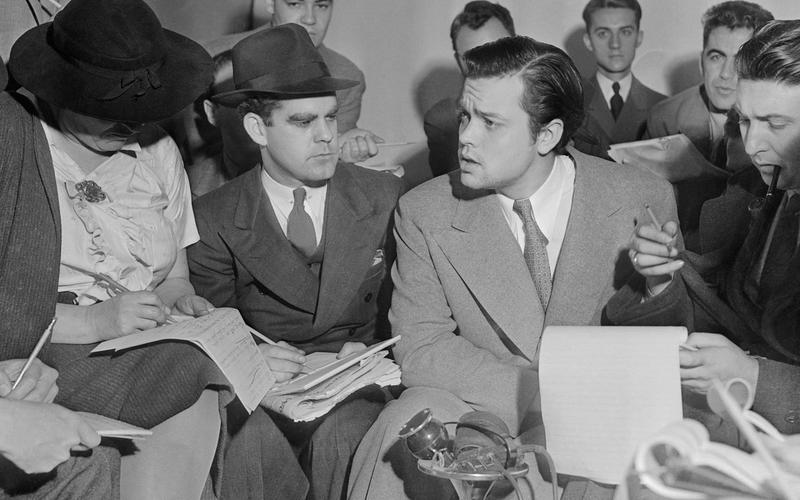 Orson Welles cercado de repórteres em 31 de outubro de 1938, um dia após a transmissão de A Guerra dos Mundos, com microfones à sua frente.