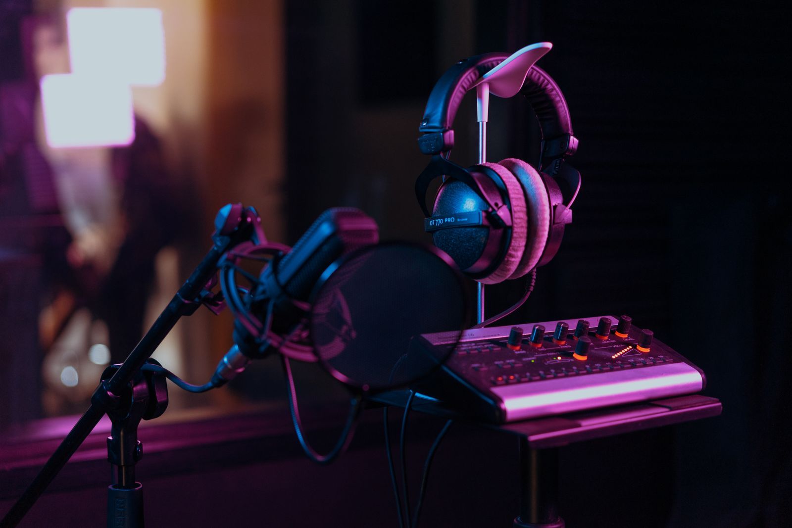 Microfone condensador profissional com filtro pop, fones de ouvido e mesa de som em estúdio escuro com iluminação cinematográfica em tons de roxo e laranja