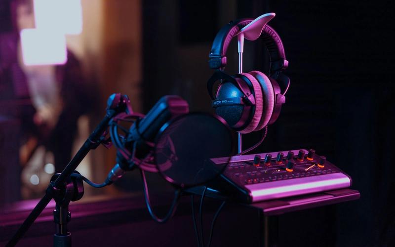 Microfone condensador profissional com filtro pop, fones de ouvido e mesa de som em estúdio escuro com iluminação cinematográfica em tons de roxo e laranja