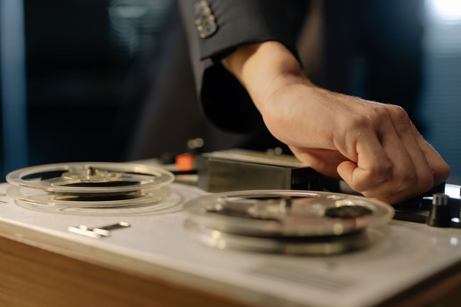 Close-up de uma mão ajustando os controles de um gravador de rolo (reel-to-reel) vintage, remetendo à gravação de jingles publicitários de rádio